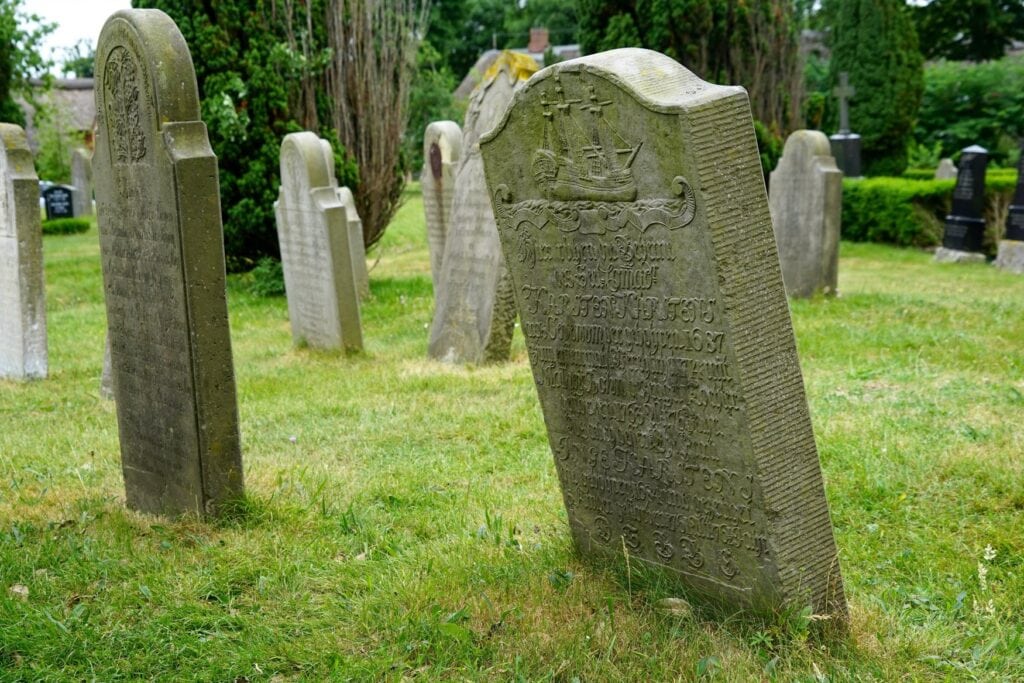 Historische sprechende Grabsteine auf dem Friedhof von Nieblum, der vordere Stein zeigt ein Segelschiff über einer Inschrift.