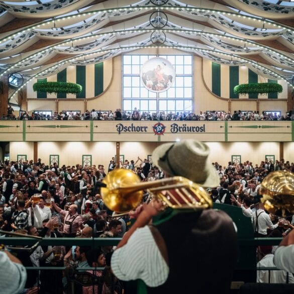 Blasmusiker mit Trompeten und Tuba spielen von der Bühne in ein volles Festzelt mit Galerie und Zeltdekoration.