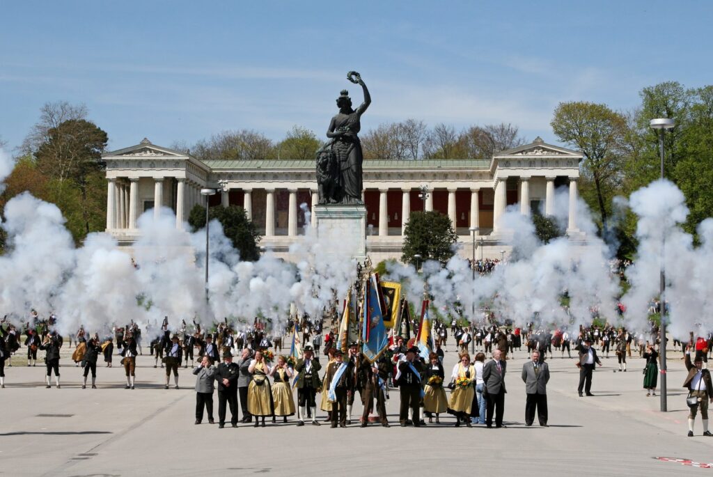 Böllerschützen geben vor der Bavaria und der Ruhmeshalle Salut, dichter weißer Rauch steigt über dem Platz auf.