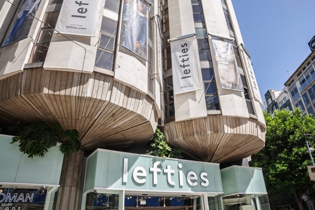 Untersicht auf ein Gebäude in Valencia mit Lefties-Filiale im Erdgeschoss, an der Betonfassade hängen Werbebanner der Marke.