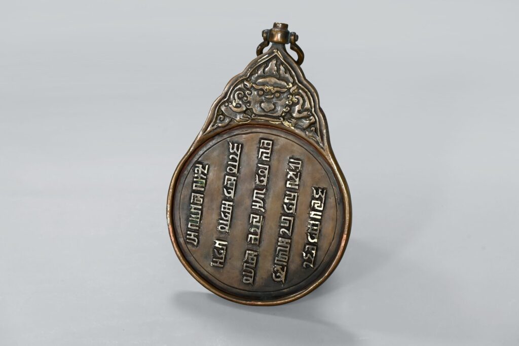 Kopie eines Paiza, eines Passierscheins des Mongolischen Reiches aus dem 13. bis 14. Jahrhundert. Der birnenförmige Metallanhänger trägt eine Inschrift in Silber, darüber sitzt ein Dämonenkopf im dreieckigen Aufsatz.