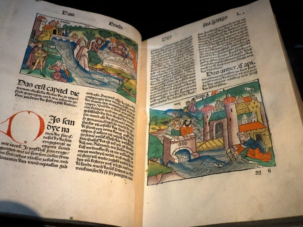 Wandern in Rheinhessen: Aufgeschlagene Gutenberg-Bibel mit gedruckten Texten und zwei farbigen Illustrationen in Mainz.
