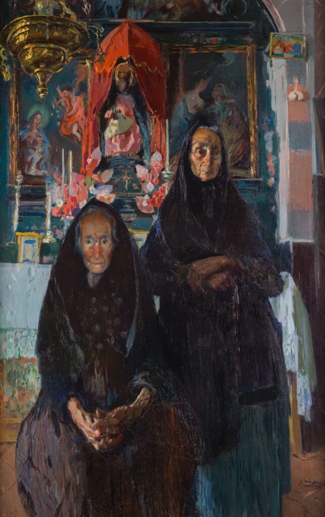Joaquim Mir, „Die Alten”, 1913: Zwei alte Frauen in schwarzen Kopftüchern und Gewändern sitzen und stehen vor einem Altar mit Marienfigur unter rotem Baldachin, Kerzen und Blumen.