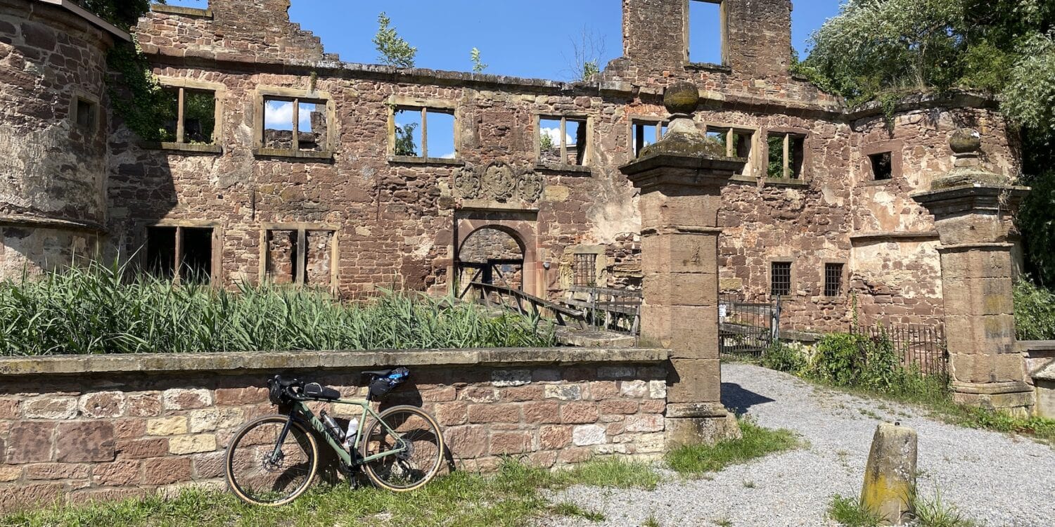 Lost Places in Baden-Württemberg: Ruine des Wasserschlosses Menzingen in Kraichtal mit verwitterten Steinmauern, leeren Fensteröffnungen und einem Fahrrad im Vordergrund.